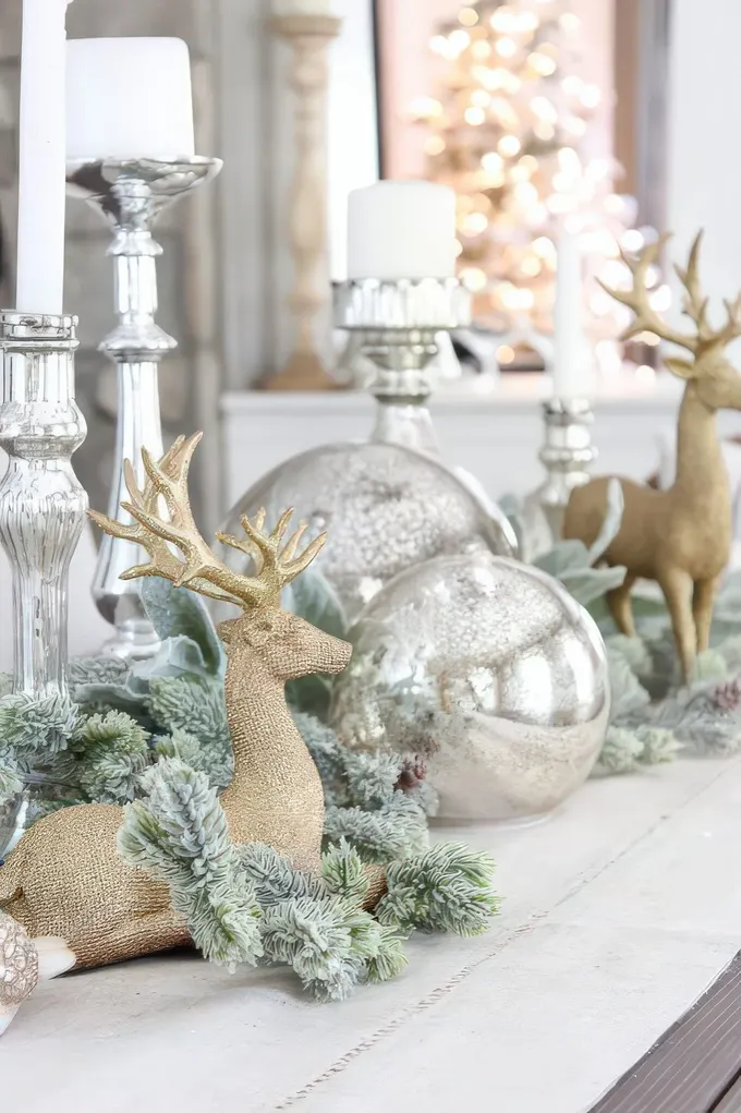 Büyük gümüş süsler, gümüş mumluklar, karla kaplı yeşillikler ve altın renkte geyiklerle nostaljik Noel dekorasyonu.