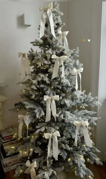 Bu kar püskürtmeli yılbaşı ağacı ışıklar ve çam kozalakları ile süslenmiş, beyaz fiyonklarla daha şık ve sevimli bir görünüm kazanmış.