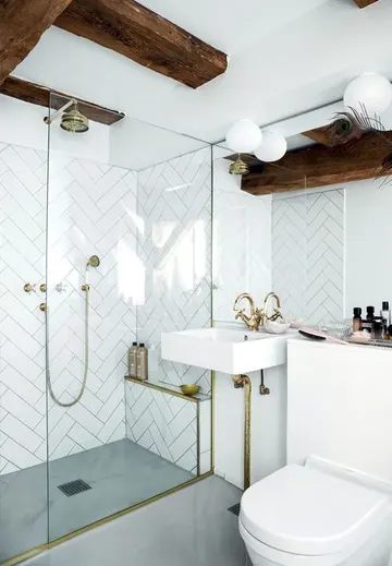 Beyaz balık kılçığı fayanslar, koyu ahşap kirişler ve lüks dokunuşlu altın armatürlü şık küçük banyo.