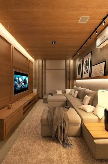 Ev sineması büyük gri köşe koltuk, TV, raflar ve sanat eserleriyle hazırlanmış; katmanlı ışık dar alanı geniş hissettiriyor.