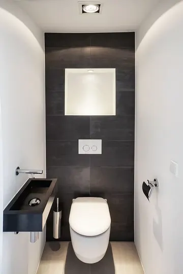 Farklı boyutlarda siyah ve beyaz fayanslarla, siyah duvara monte lavabo ve bazı ışıklarla minimalist bir misafir banyosu.