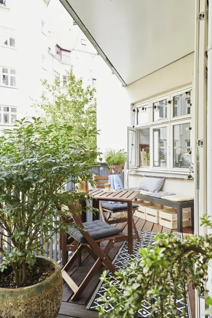 Şekilli balkon saksıdaki yeşillik, boyalı yemek takımı, bir bank ve halıyla dekore edilmiş.