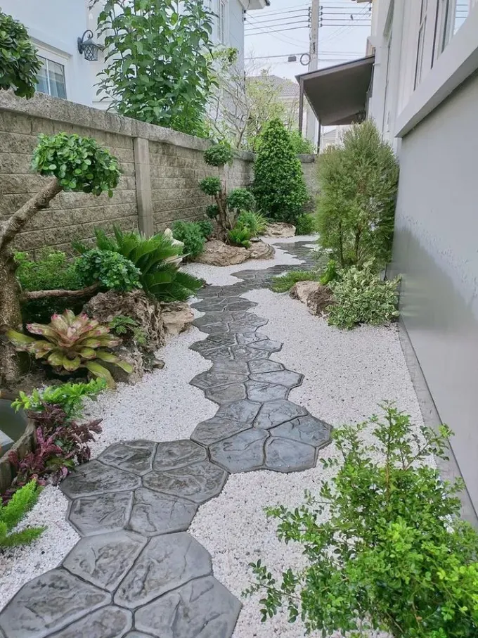 Dar yan bahçe beyaz çakıl, beton taş basamaklar, yeşillik, sukulentler ve ağaçlarla yapılmış.