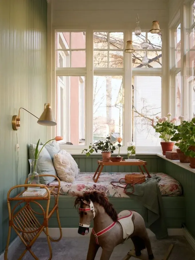 Bu vintage balkon, yumuşak yeşil tonlarında, içinde bir sedir, masa ve saksı çiçekleri var.