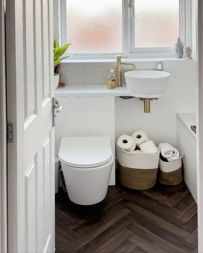 Bu modern küçük banyo, şık duvara monte tuvaleti, minimalist beyaz lavabo ve kompakt tezgahıyla alanı verimli kullanıyor. Pirinç musluk şıklık katıyor.