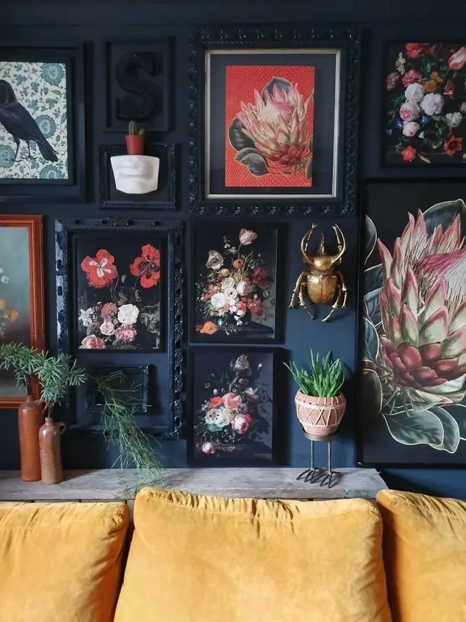 Sanat eserleri, bitkiler, monogram ve altın bir böceğin yer aldığı etkileyici karanlık tonlarda galeri duvarı.