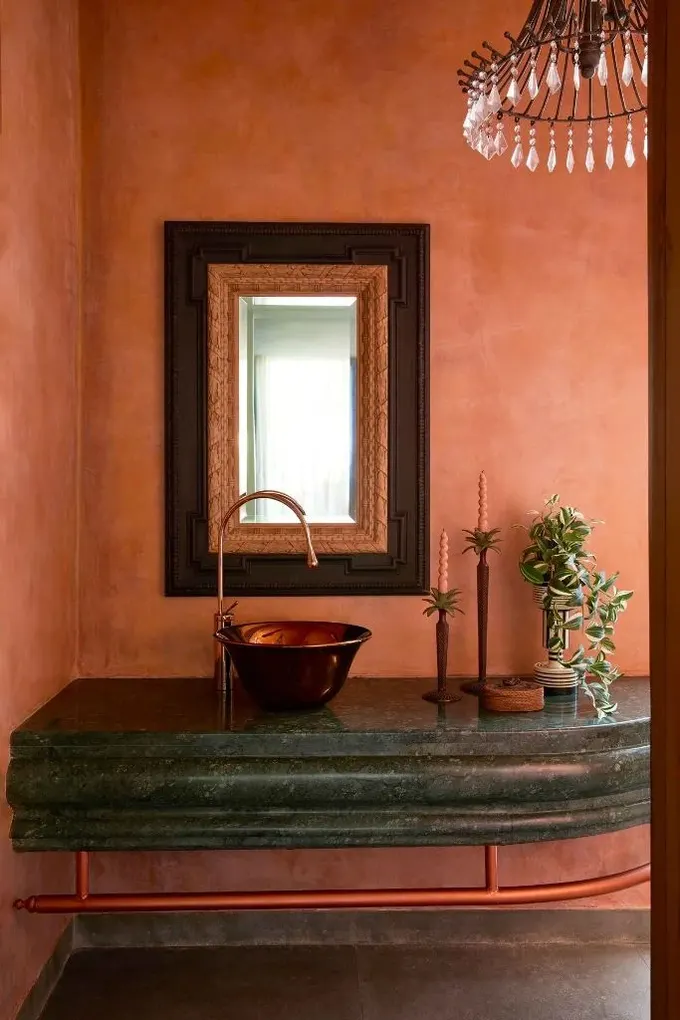 Zarif mekân, dokulu terra cotta duvarları ve metal kaseli koyu yeşil bir lavabo dolabını sergiliyor.