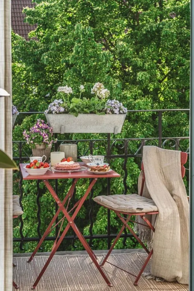 Balkon çiçeklerle ve kırmızı metal şık mobilyalarla düzenlenmiş, dayanıklı malzeme kötü hava koşullarına dayanır.