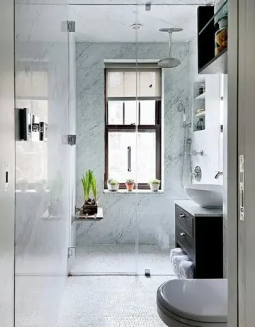 Duşta mavi taş karolar, koyu renk lavabo, saksı bitkileri ve gömme raflar bulunan küçük banyo.