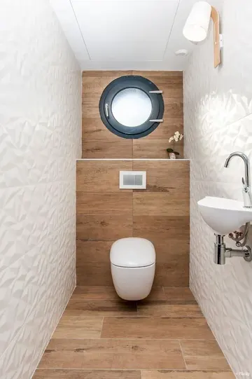 Ahşap görünümlü ve geometrik beyaz karolar, pencere, duvara monteli lavabo ile modern misafir tuvaleti.