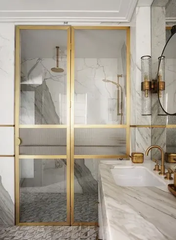 Beyaz mermer karo ve lavabo ile kaplı zarif bir banyo; cam ve altın kapılı duş alanı ve altın armatürler bulunuyor.