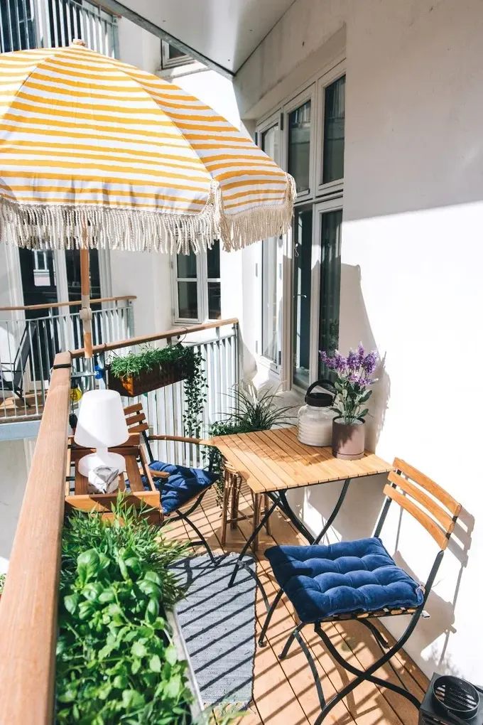 Parlak şemsiye, bol yeşillik ve rustik tarz mobilyalarla yazlık balkon hazır halde.