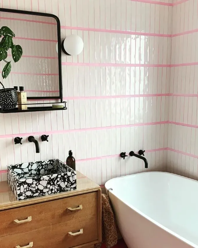 Banyo, siyah armatürler, taş lavabo ve pembe derzle modern bir hava kazanıyor.