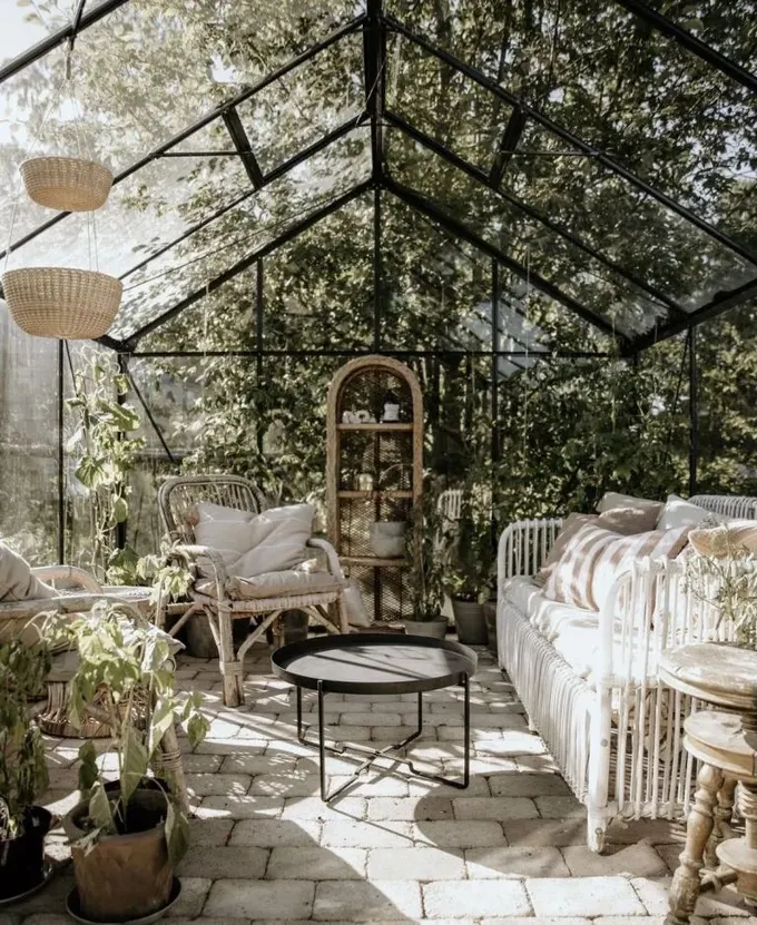 Sera, bir daybed, bazı sandalyeler, masalar ve yeşilliklerle güzel ve nötr tonlarda bir dış mekan odası.