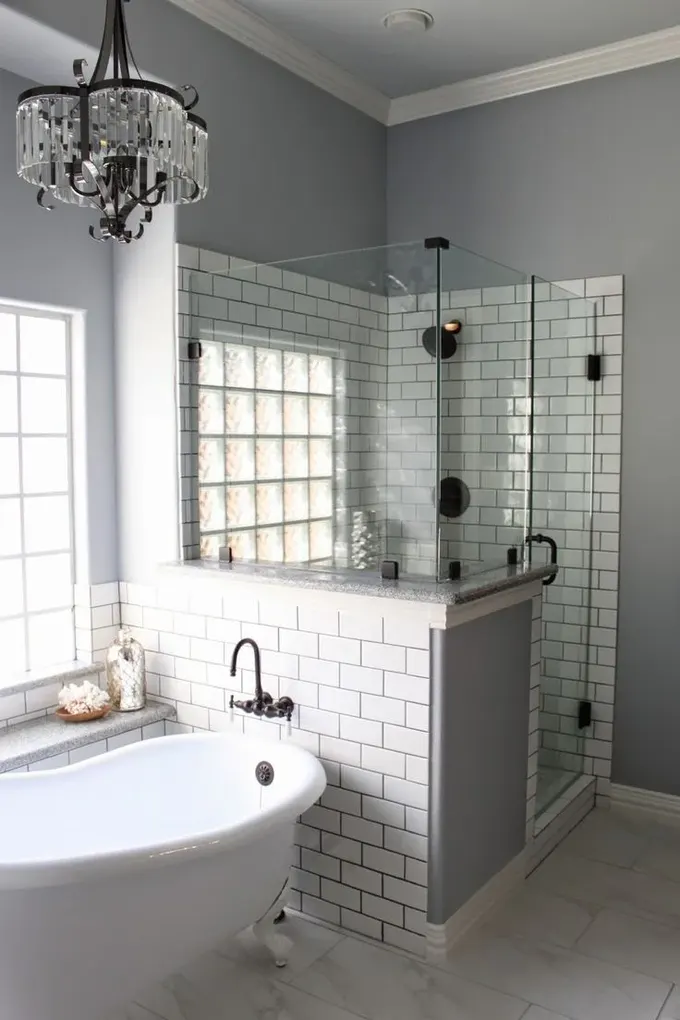 Gri banyo, beyaz metro fayanslar, yarım duvarlı duş alanı, kristal avize ve vintage küvet.