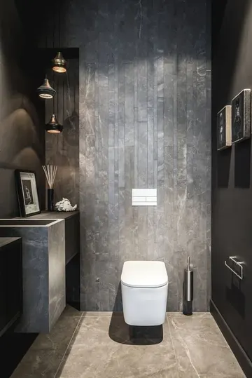 Beton ve taştan yapılmış endüstriyel misafir tuvaleti, sarkıt lambalar, taş lavabo ve bazı sanat eserleri.