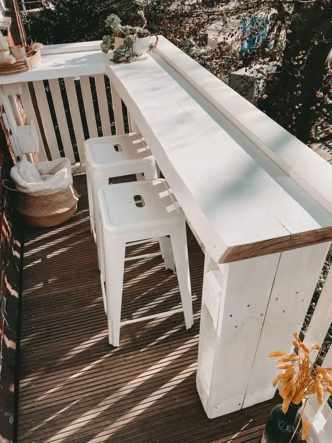 Küçük balkon, beyaz köşe masa ve birkaç tabureyle düzenlenmiş. Bu masa içecek, yemek, çalışma veya bahçecilik için ideal.