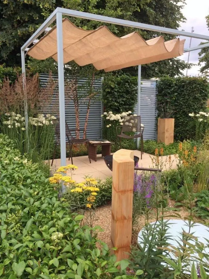 Pergola, kütüklerle uyumlu keten bir örtüye ve etrafa serpilmiş çiçeklere sahip, tazelik katıyor.