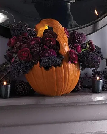 Oyulmuş ve koyu renkli çiçeklerle doldurulmuş kabak, şık ve gösterişli bir Halloween dekor fikri, etkileyici görünüyor.