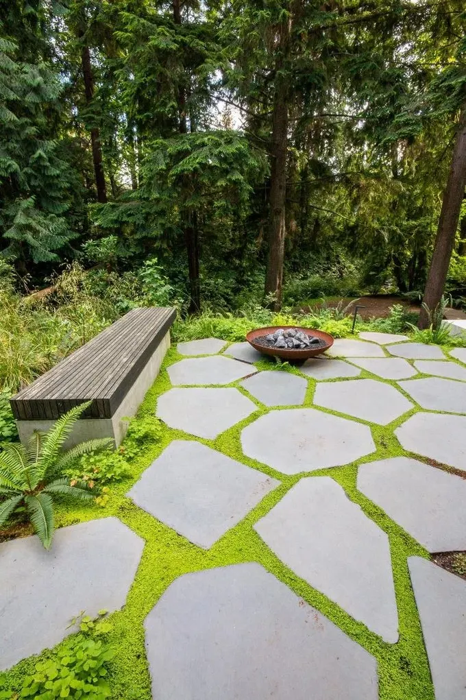 Parlak yosun arka planında öne çıkan büyük taşlarla oluşturulmuş bu modern verandayı çok seviyorum. Modern oturma bankı ve ateş çanağı alana şıklık katıyor.