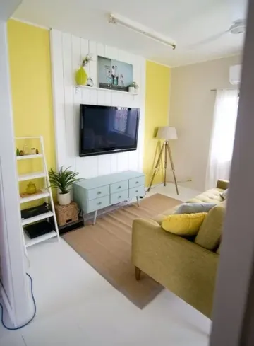 TV'nin öne çıkmasını sağlayan ve kabloları gizleyen beyaz duvar aksanlı aydınlık bir oturma odası.