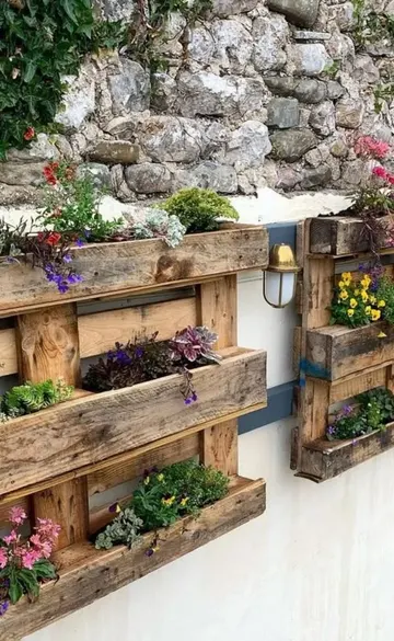 Boyalı paletler çit üzerine asılı bahçe, çeşitli çiçeklerle mekanı canlandırıyor.