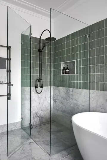 Beyaz mermer ve yeşil fayanslı modern banyo, oval küvet, cam kapaklı duş alanı.
