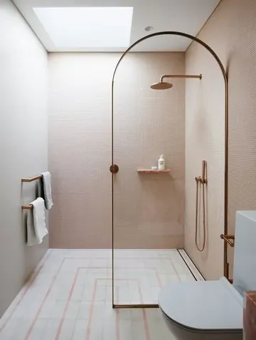 Pembe mini karolarla kaplı, nötr-pembe zemin, duş üstünde çatı penceresi ve pirinç dokunuşlu küçük özgün banyo.