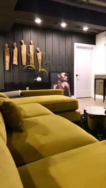 Ev sineması siyah duvarlar, kalıplar, bazı sanat eserleri ve hardal renkli bir koltukla tamamlanmış.