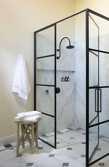 Taba renkli duvarlar, beyaz mermer ve siyah beyaz karolarla güzel nötr banyo, siyah çerçeveli duş kapısı ve tabure.